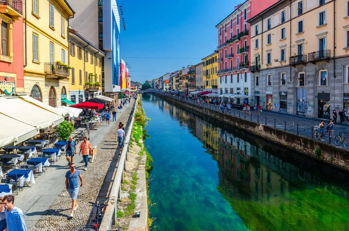 Colorful store fronts and people walking along the Navigili Canals in Milan on a warm day. 
