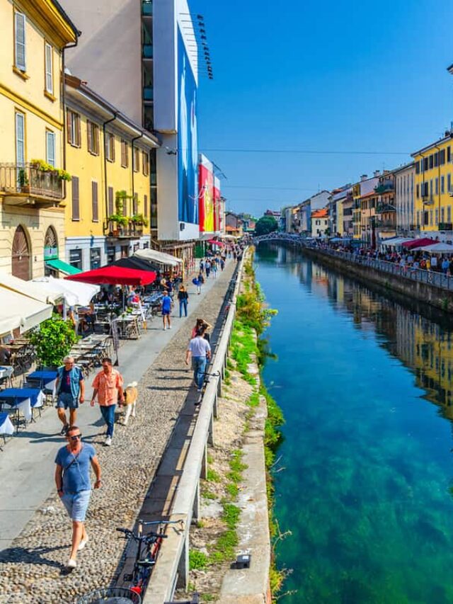 Colorful store fronts and people walking along the Navigili Canals in Milan on a warm day.