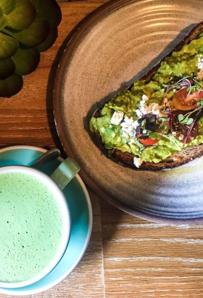Aerial view of my Matche latte and avocado toast from Bluestone Lane on the Upper East Side. It sits on a wooden table. 