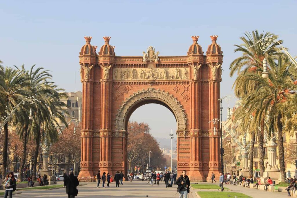 A brick arch with palm trees and turrets tops in Barcelona. Do Barcelona solo travel and walk through this incredible arch.