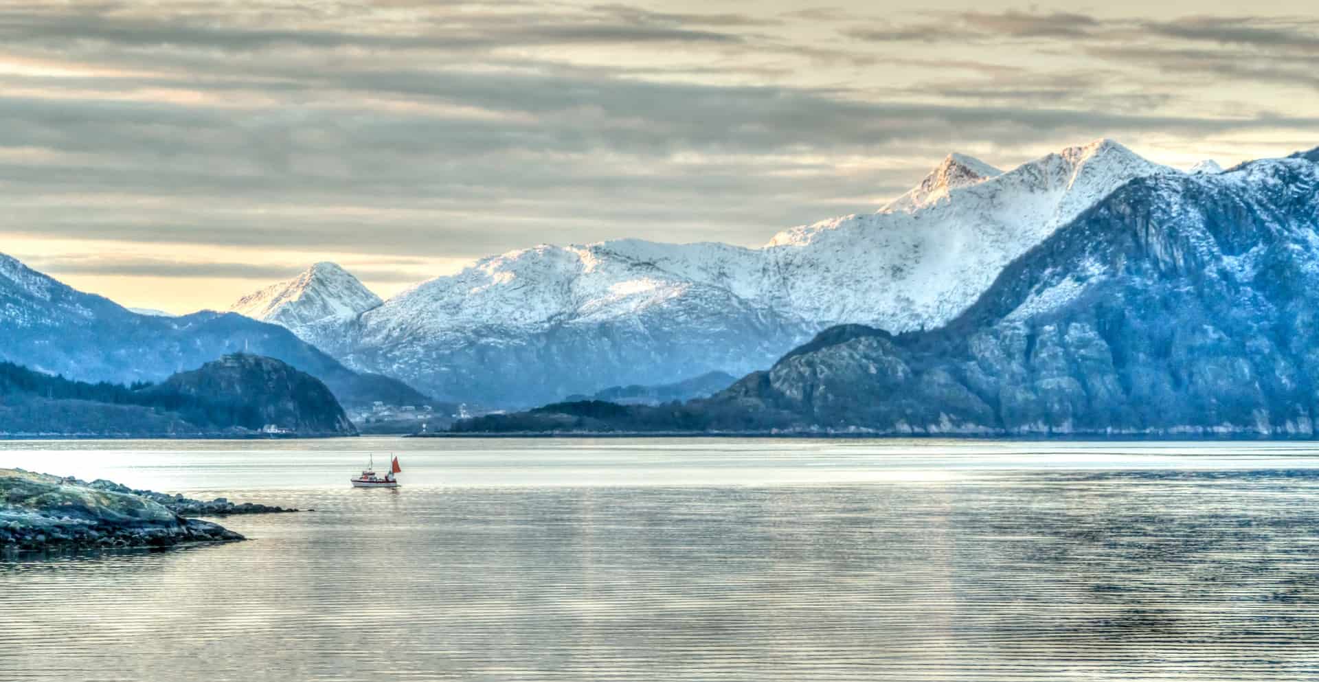 The snow coated hills and a boat on the water showing just why one of the best Norway travel tips is to visit during winter.