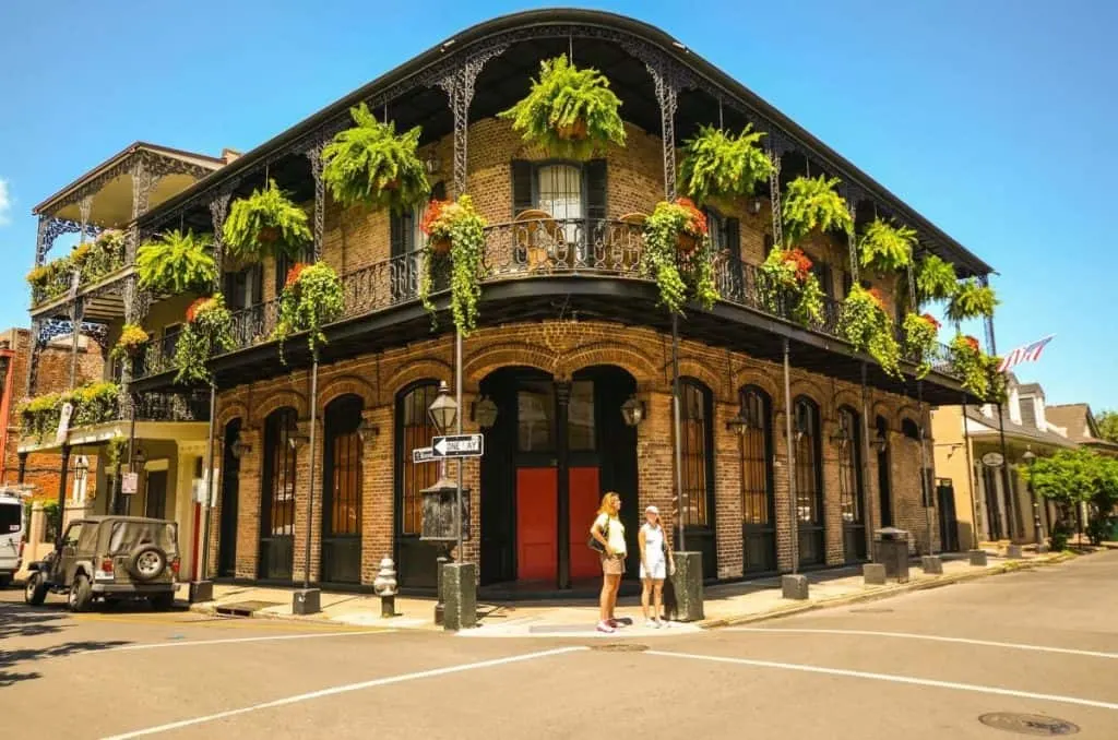 View of a historic home in the French Quarter with a covered porch with tons of hanging plants. You can also see two women standing out front. 