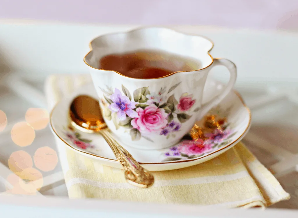 A floral tea cup with tea on a floral saucer with a gold spoon at the Alice and Wonderland themed restaurant in NYC