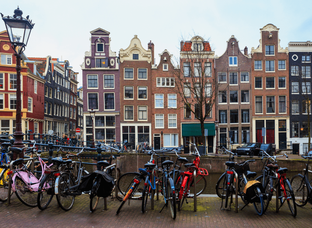 A line of bikes sitting on a bike rack next to a set of row houses in Amsterdam. 
