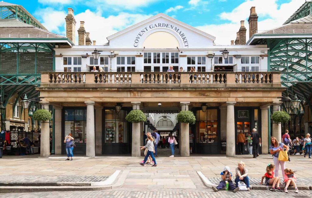 Exterior view of Covent Garden and the people sitting outside of the historic glass building at its center. 