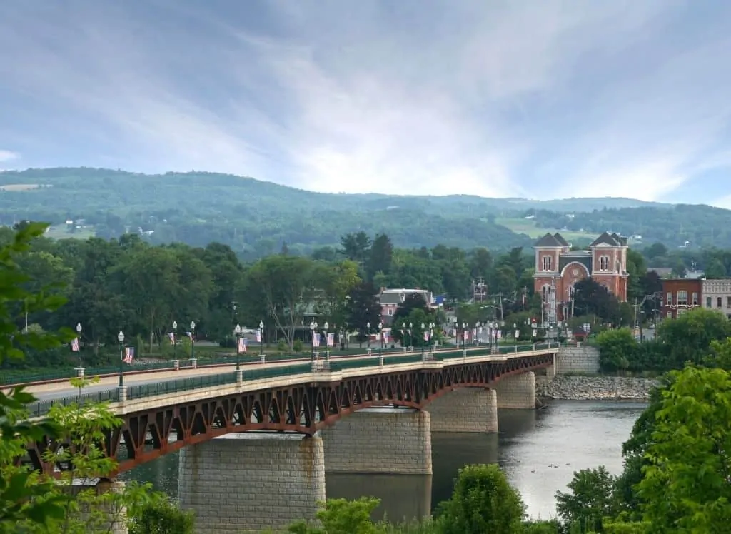 A view of the bridge across the Susquehanna River in Owego, NY with the brick buildings in the distance and the gorgeous green hills. This is one of the cool  romantic getaways in Upstate New York