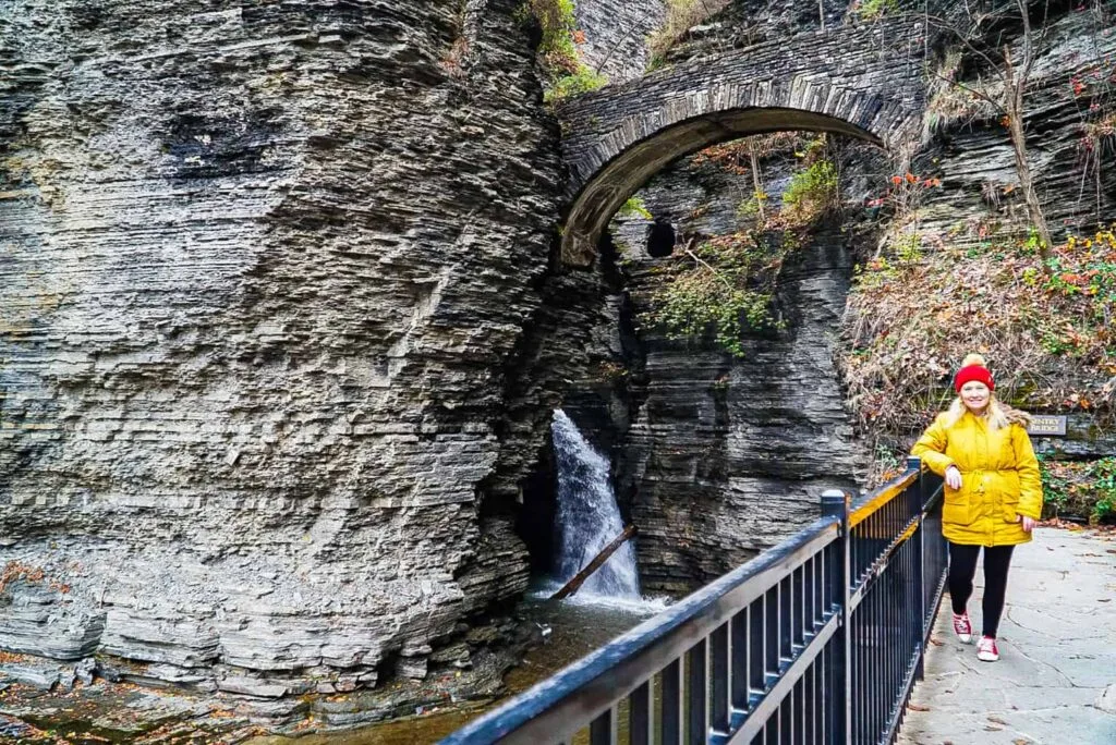 View of me in a yellow coat and red hat standing in front of Watkins Glen in the winter. 
