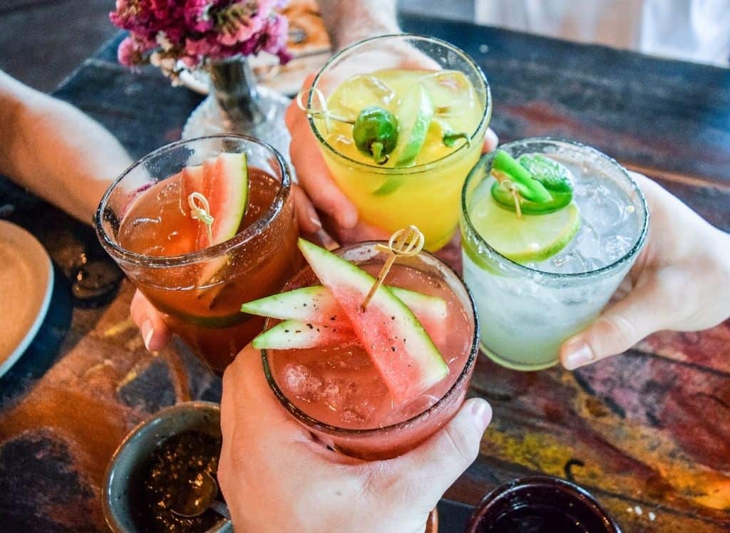 Four people holding their cocktails together at a bar. 