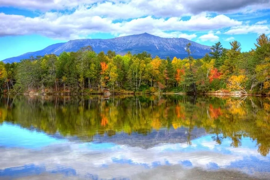 A view of Mount Katahdin in Maine in the distance with the reflection of the autumn colored trees in the water. This is another cool part of the scenic drives in Maine.