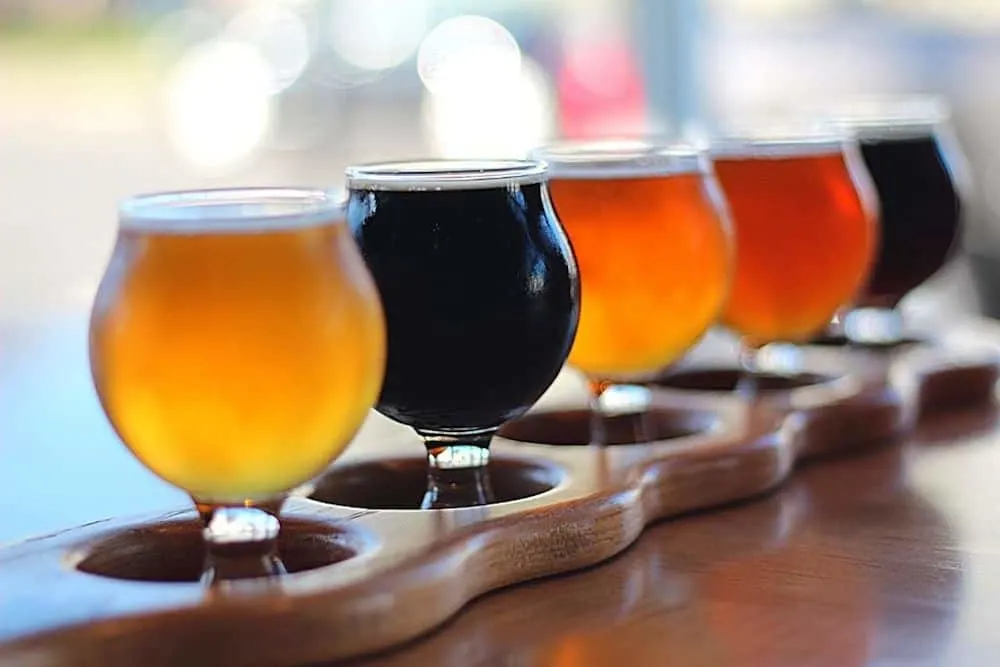 A flight of four different beers that range from light to dark. The beers sit in round glassed on a wood bar.