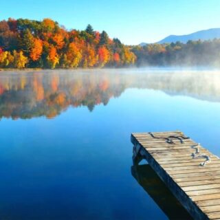 A lake in Vermont with a dock and fall foliage all around it.