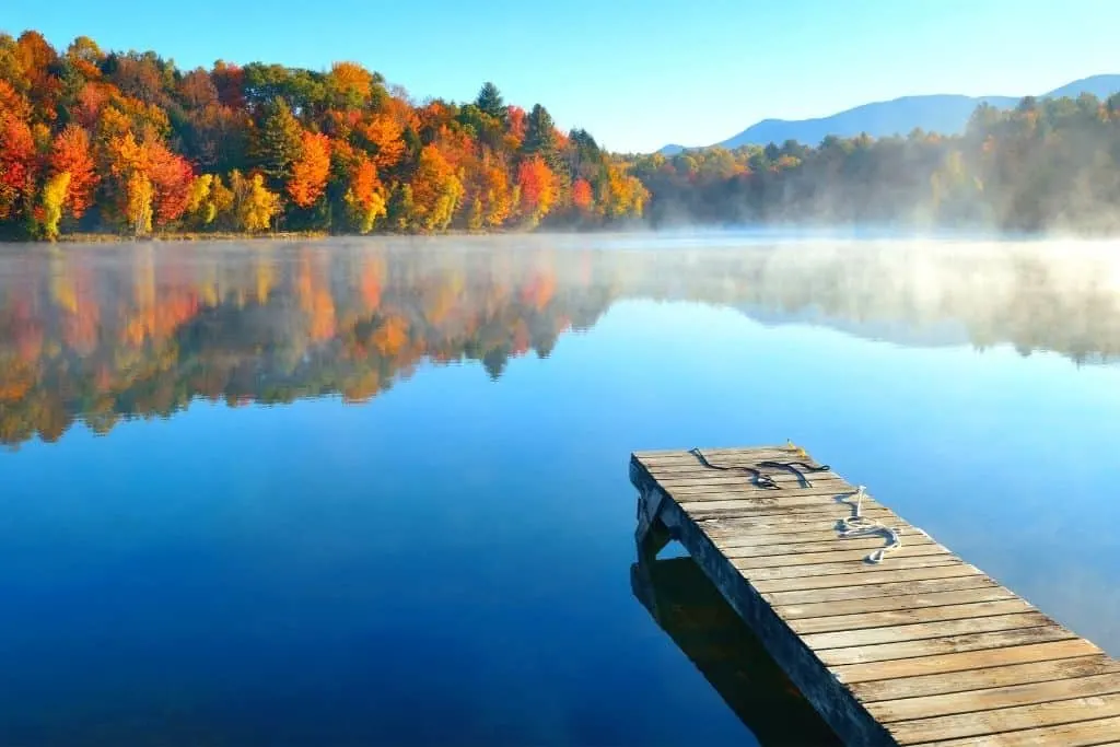 A lake in Vermont with a dock and fall foliage all around it. 