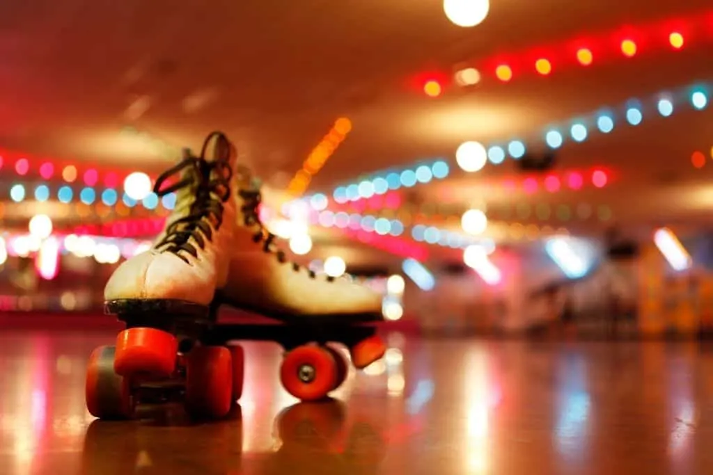 Two white roller-skate with pink stoppers and wheels at a roller disco.