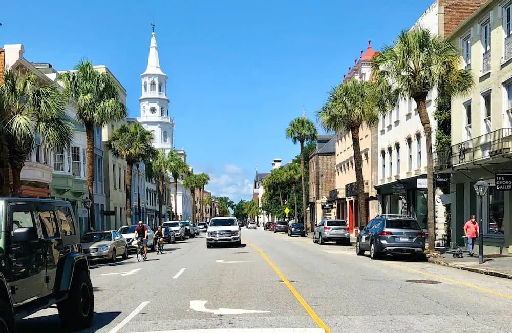 People riding their bikes and cars driving through the center of Charleston, South Carolina. 
