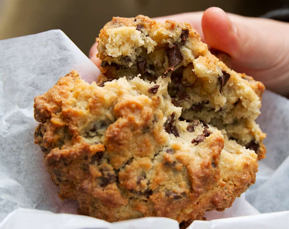 A woman holding a chocolate chip walnut cookie with wax paper around it from LeVain Bakery.
