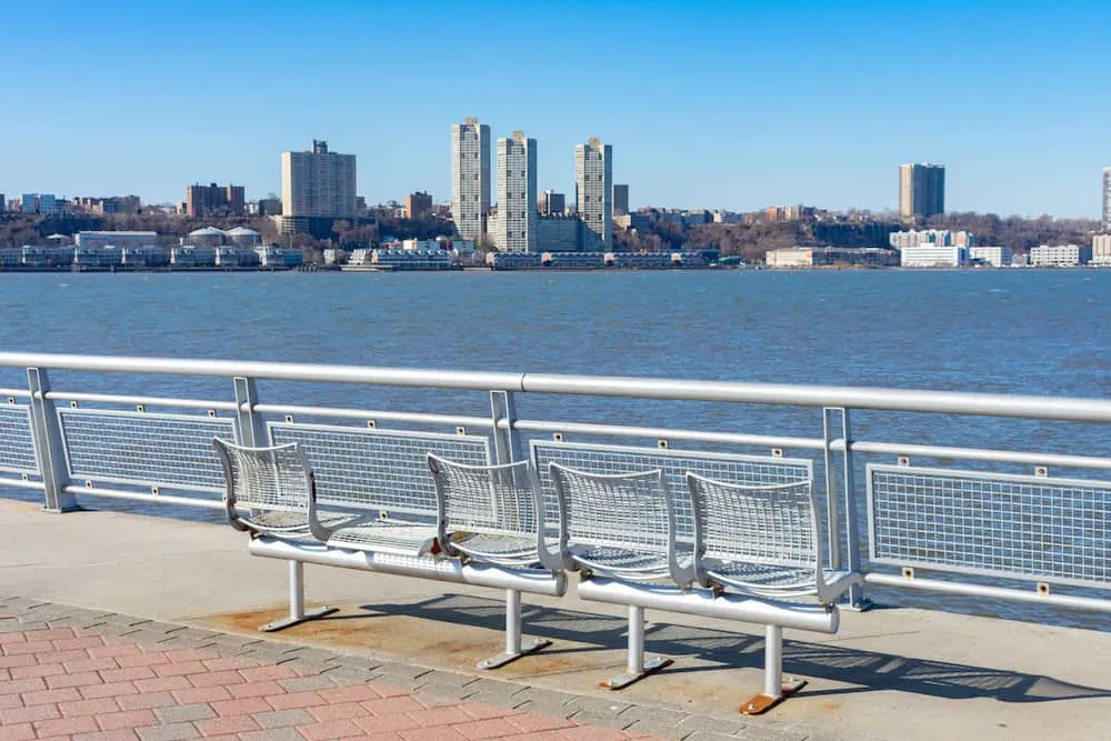 An empty metal bench at Pier I facing the Hudson River in Lincoln Square of New York City with a clear blue sky