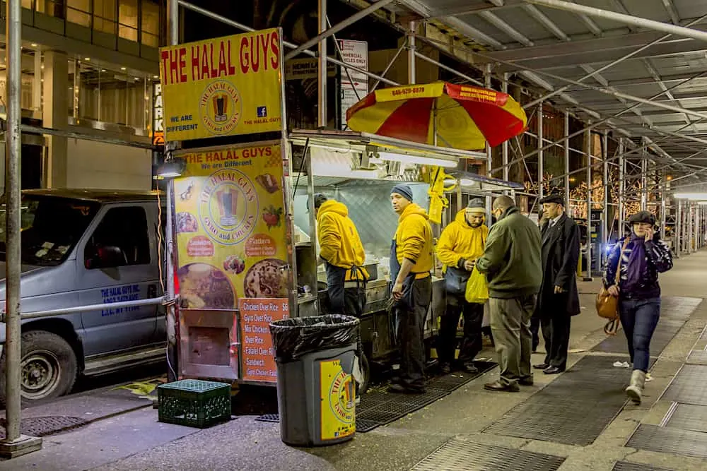 The Halal Guys, a street vendor is seen selling Halal food in Manhattan as a woman walk by talking on her cell phone.