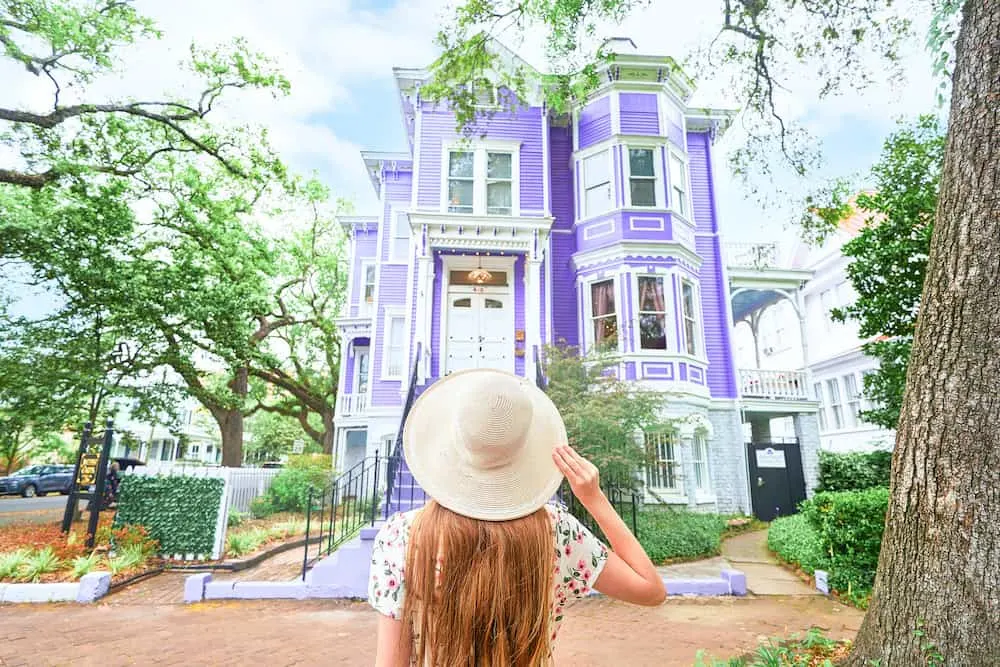 Woman in a hat standing in front of a purple house in Savannah, Georgia. 