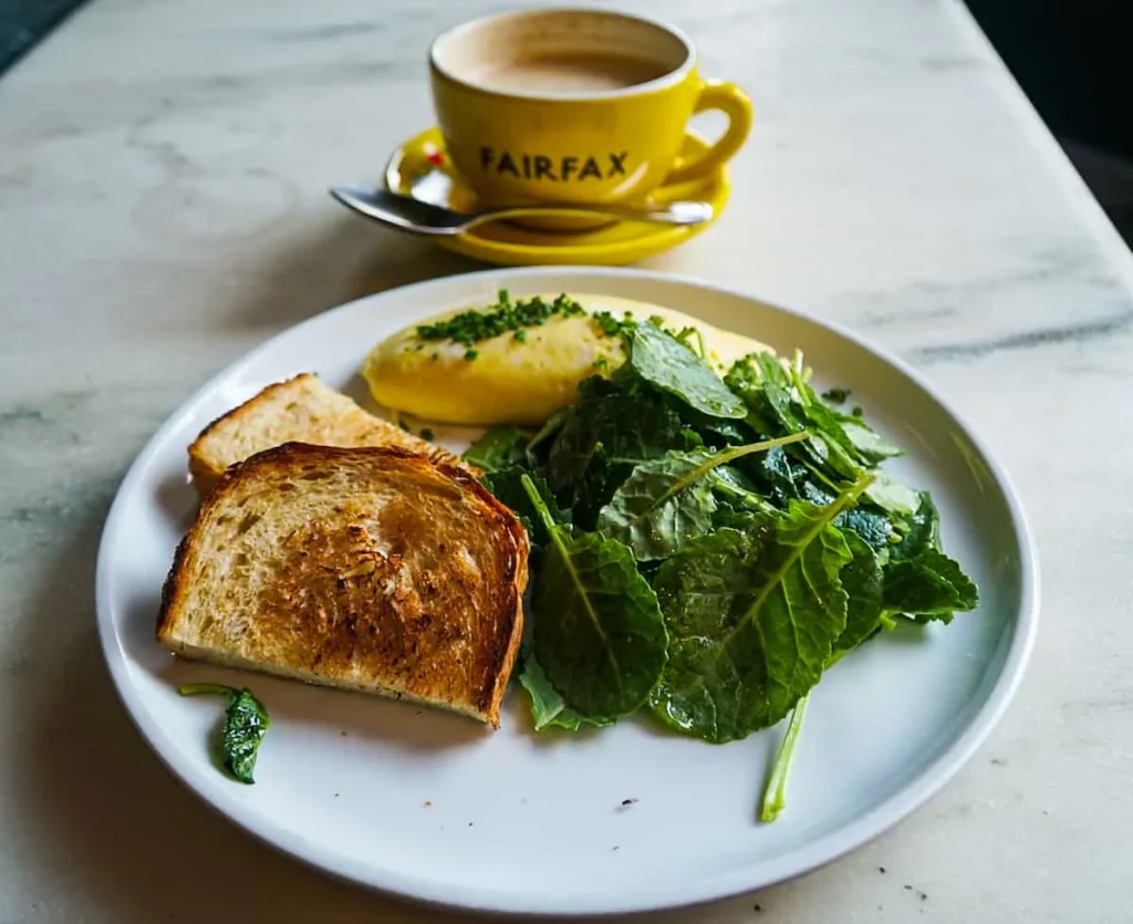 A small omelette with a kale salad and bread and a latte in a yellow mug from Fairfax