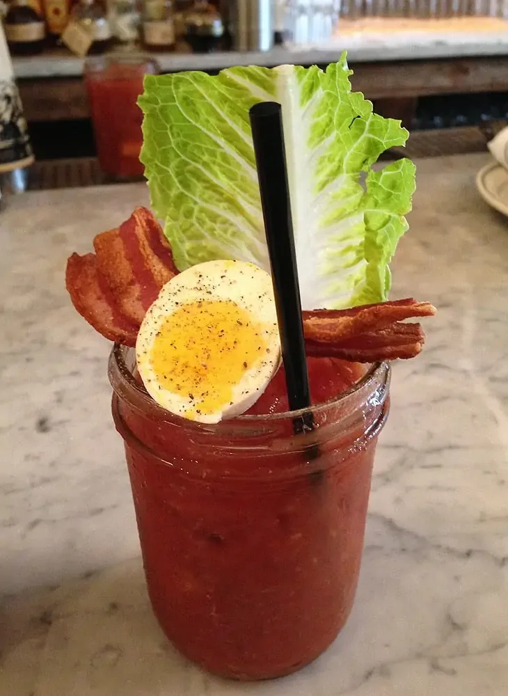 A drink with an egg, a piece of lettuce and a piece of bacon balanced on the rim of the glass at one of the best brunch spots in NYC,