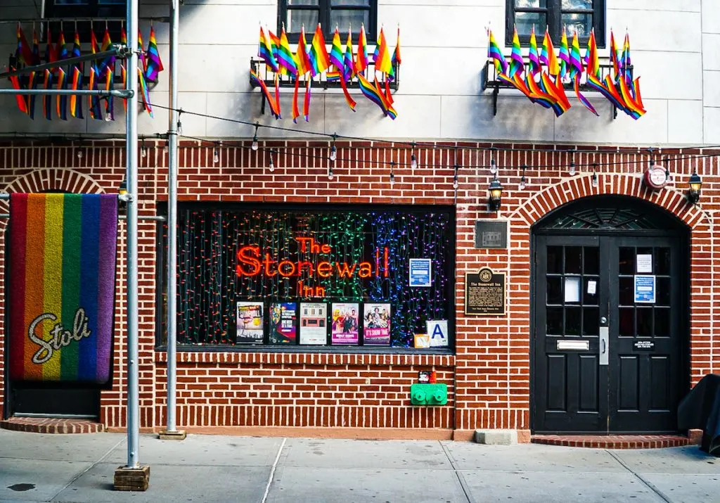 A view of the brick exterior of the Stonewall Inn in Greenwich Village. It has an arched door and red letters on the window that say, "The Stonewall Inn". 