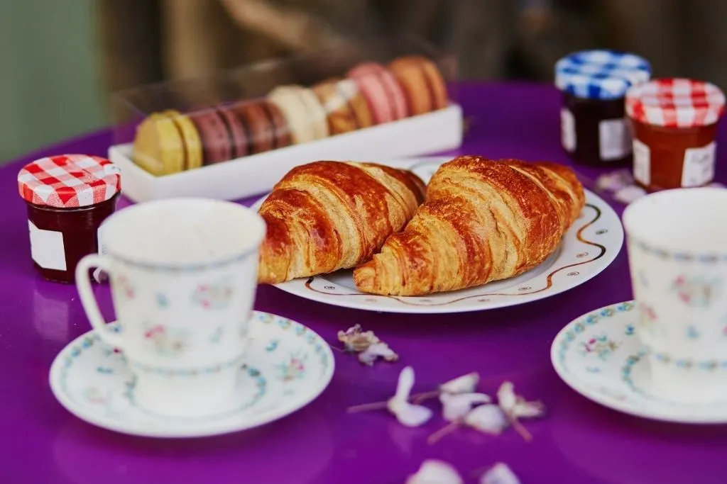 Croissants on a plate with jam and macarons in the background on a purple tablecloth. One of the  traditional foods in Paris. 