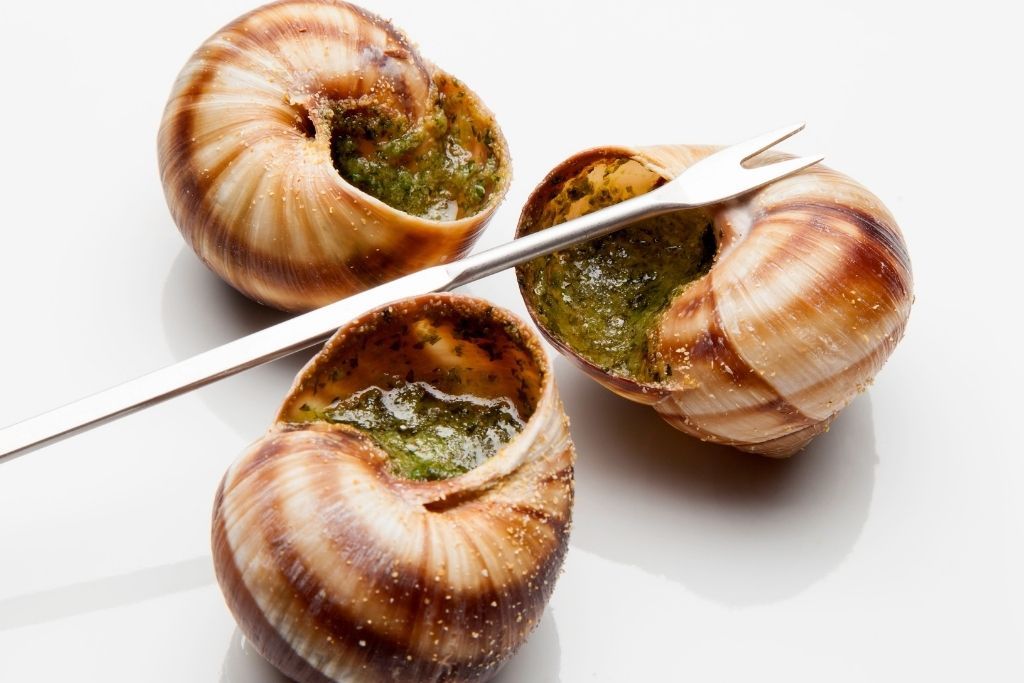 Three traditional escargot with a small fork that is a famous food in Paris.  
