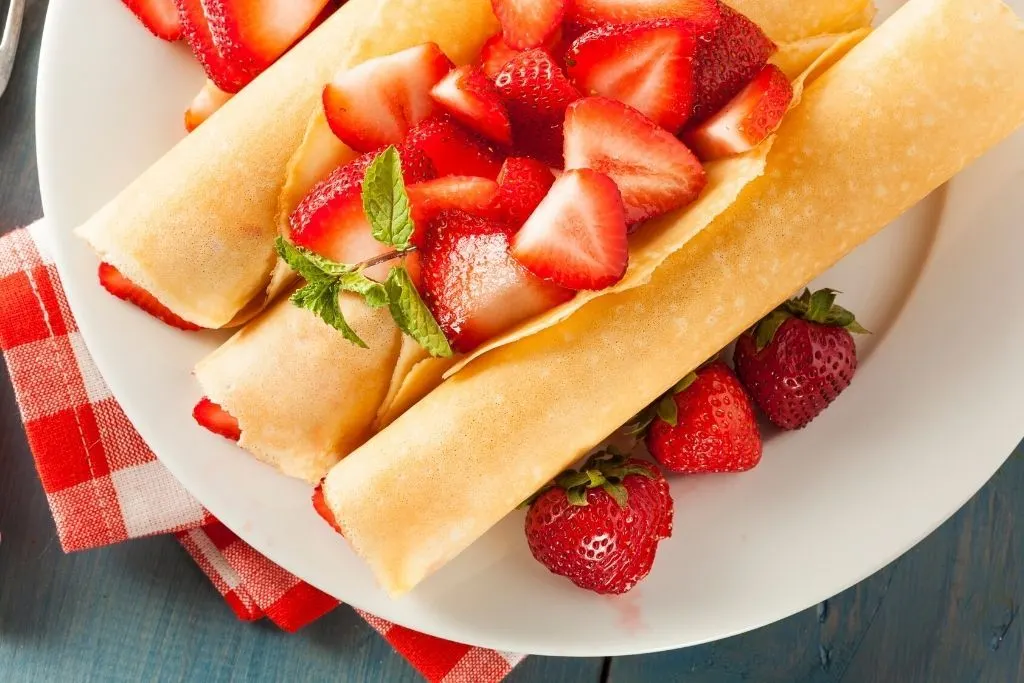 French crepes with strawberries on top of a white plate. A famous food in apris.