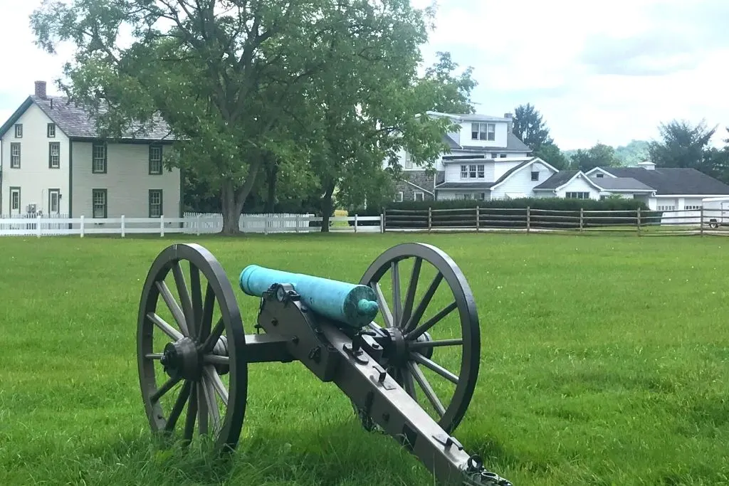 View of a historic cannon and some old farmhouses in Gettysburg, PA, the first stop on your New York to Los Angeles road trip. 