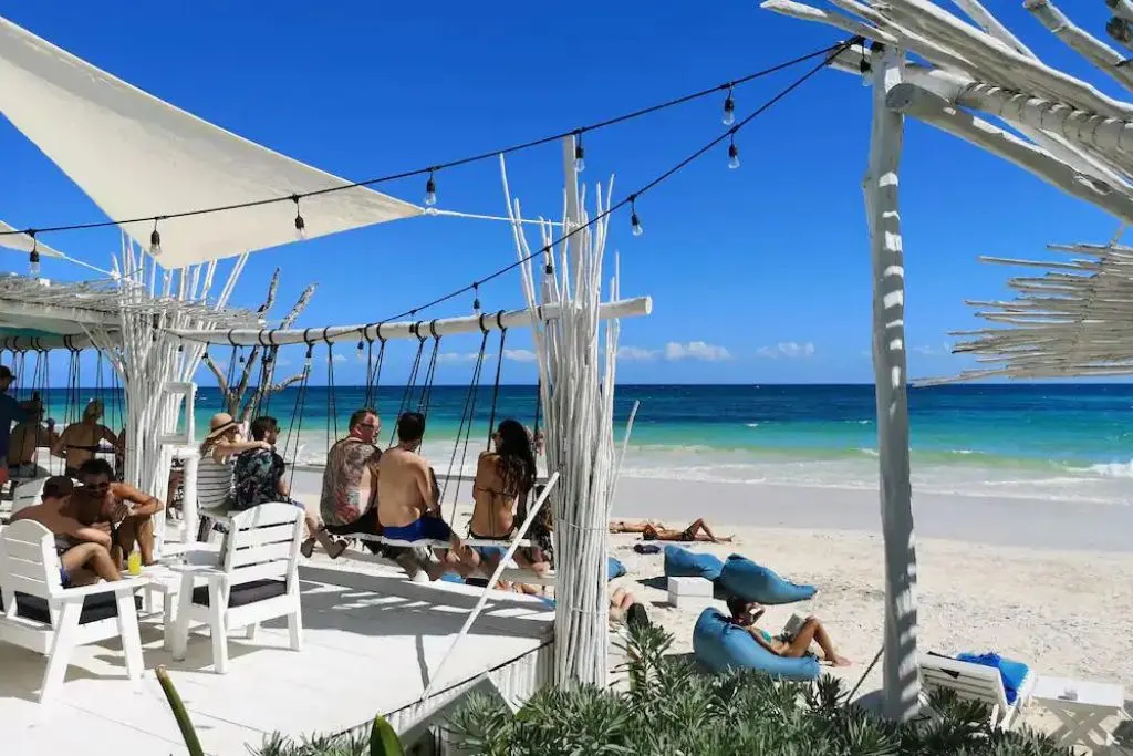 Guests sitting on swings and hanging out at Coco Tulum, one of the top beach clubs Tulum has to offer. 