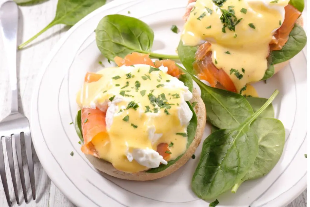 Eggs Benedict made with house-cured salmon and on a white plate with some greens. 