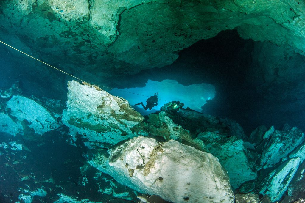 A scuba diver exploring the deep waters and caves of Cenote Jardin del Eden. 
