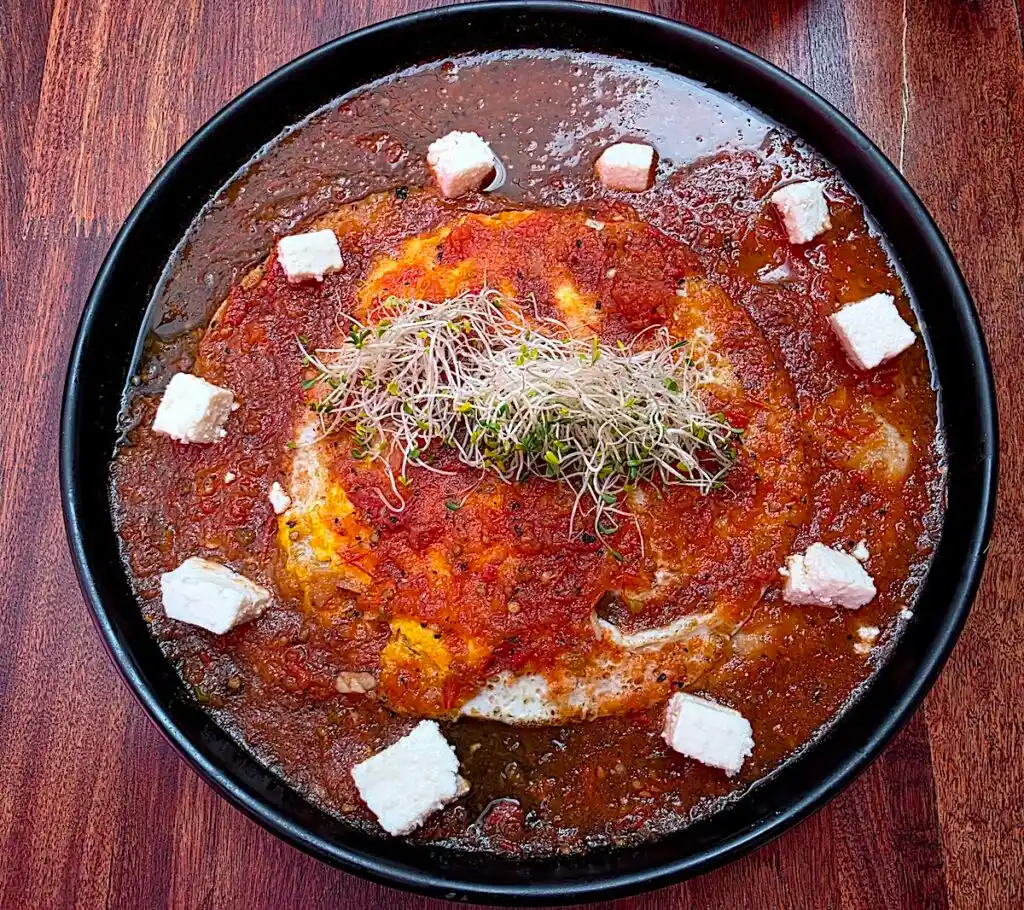 Aerial view of two eggs covered in ged sauce with cubes of white cheese around the edge of the black plate. 