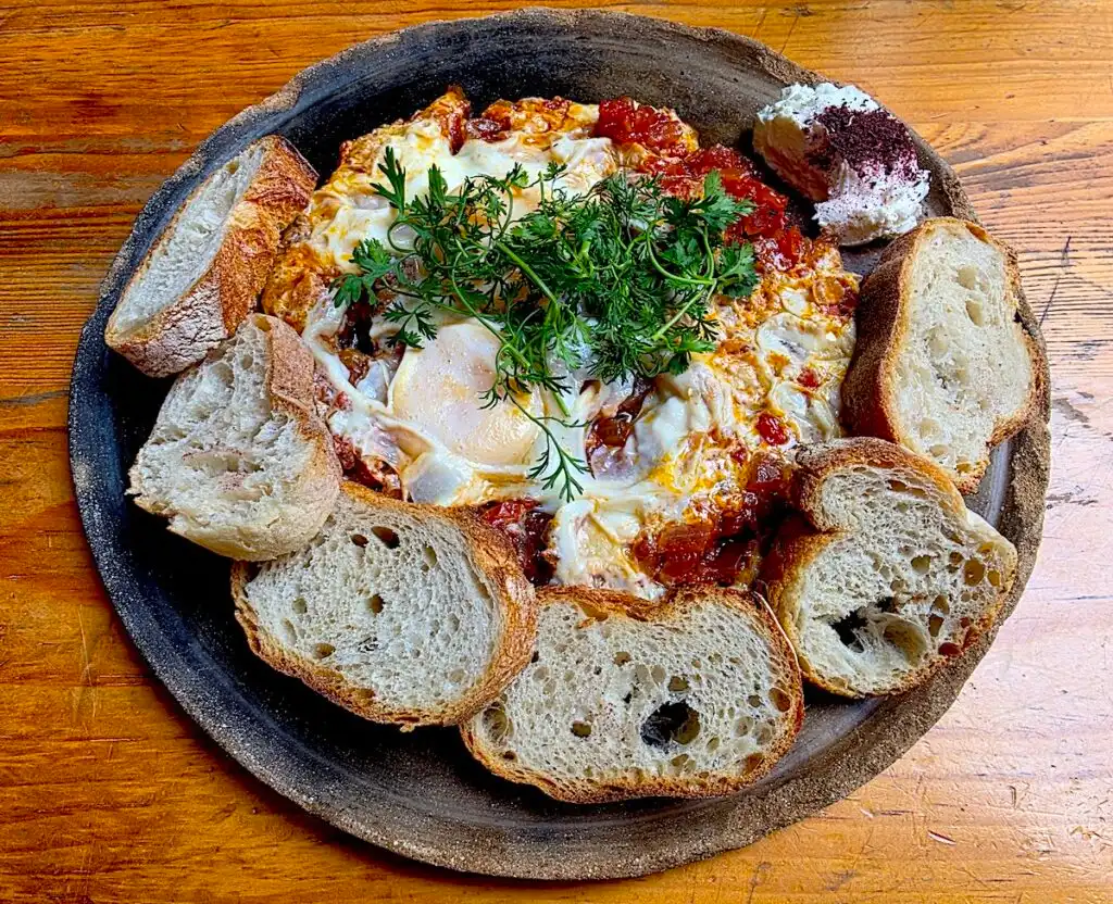 Aerial view fo Shakshuka surrounded by small pieces of bread and cheese on the side from Boulenc. 