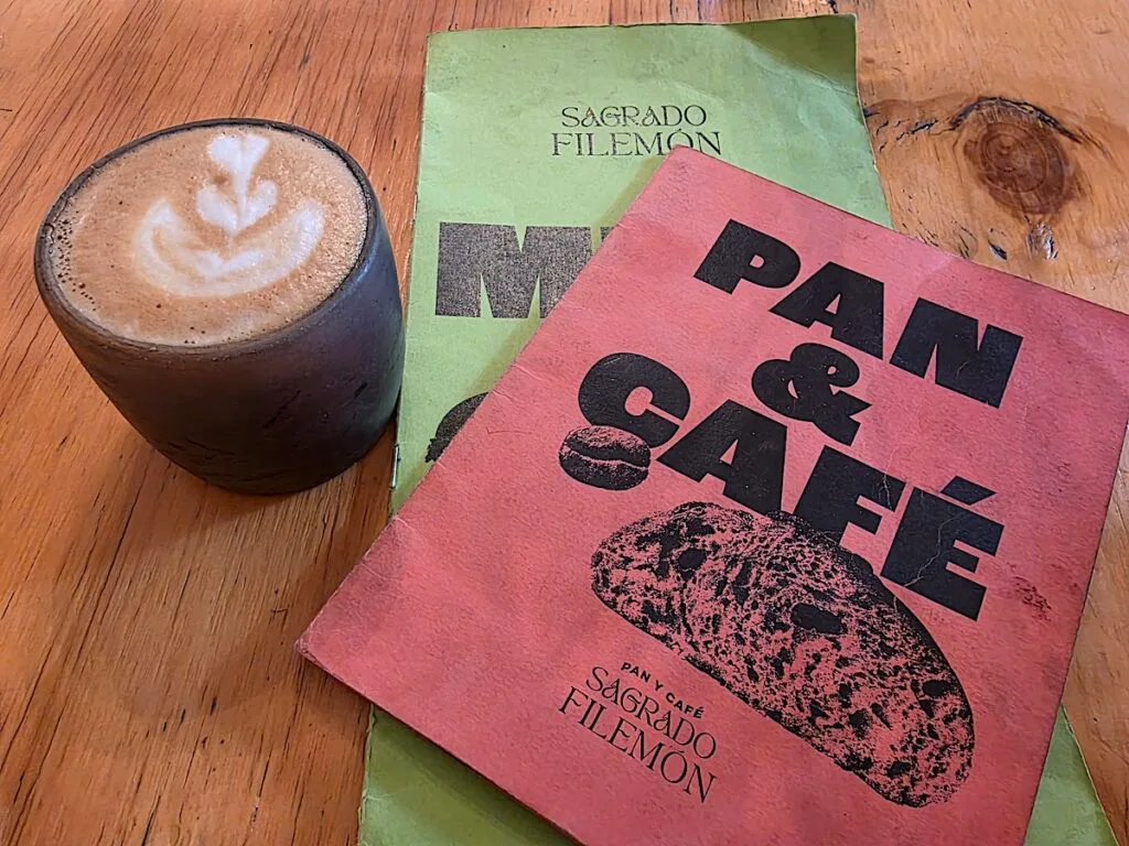 View of a latter in a small black cup with a green and pink menu to the right with the name of the restaurant on it. 