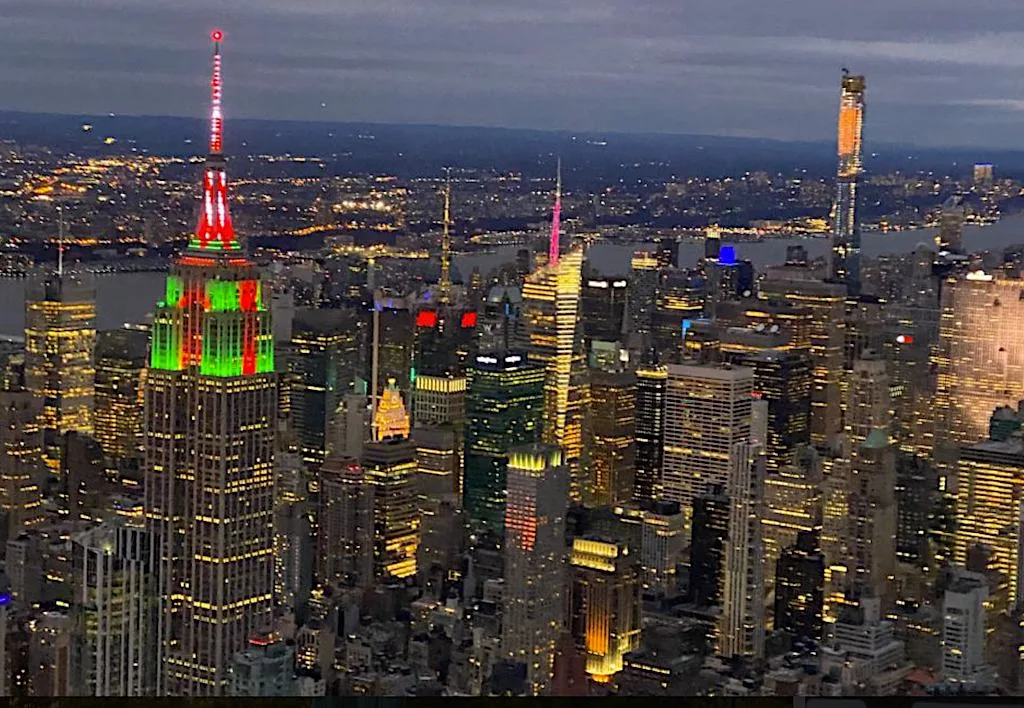 An aerial view of New York City at night with the Empire State Building glowing with Christmas colors. 