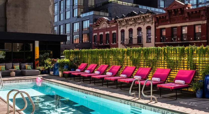 Pink lounge chairs surrounding an outdoor pool at one of the best manhattan hotels with a balcony and a pool. 