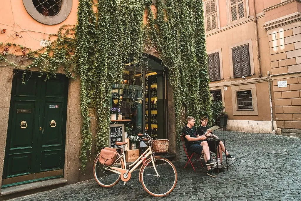 Two guys sitting in front of.a cafe in Rome covered in Ivy. 