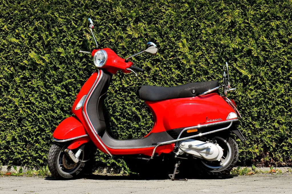 A red vespa in front of a hedge in Rome. 