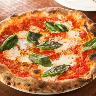 View of a Margherita pizza with green basil leaves on top and cheese and red tomato sauce.