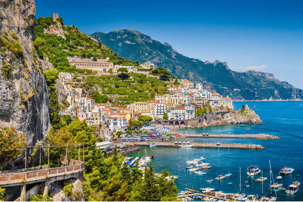 View of the Amalfi Coast with white houses along a rugged, mountainous coast with bright blue water during one of the best Pompeii day trips from Naples.