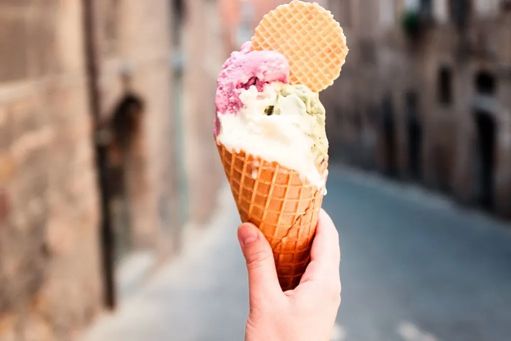 Woman holding gelato in a cone with a cookie coming out the top on the streets of Italy. 