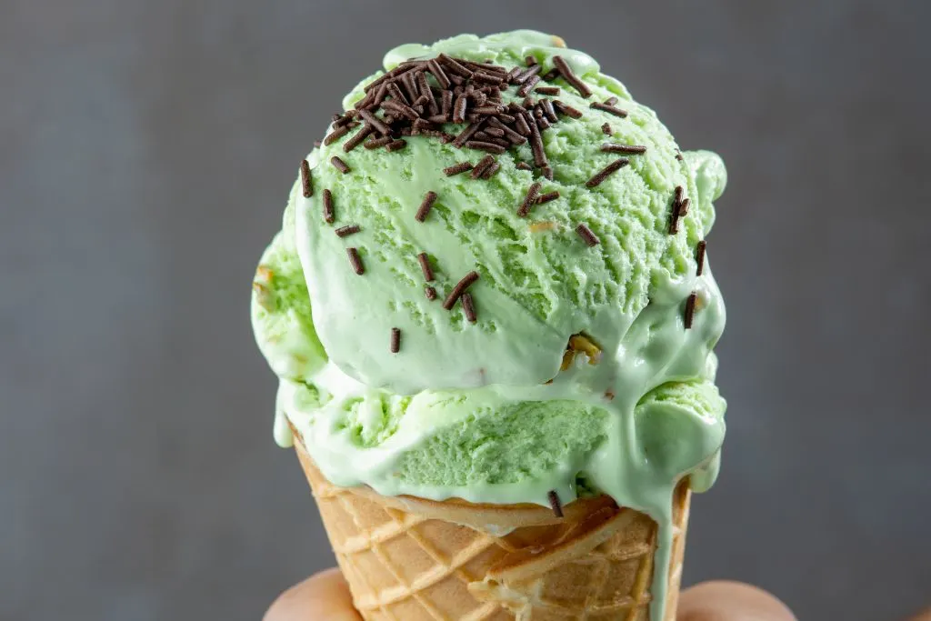 Pistachio gelato in a cone with chocolate sprinkles on top. 