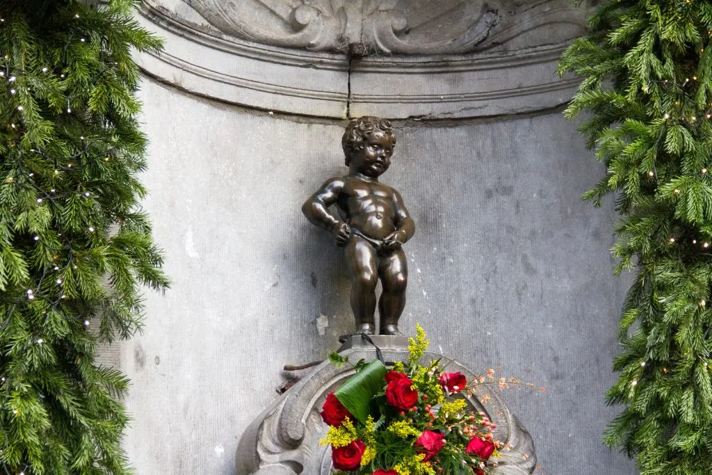 View of a statue of a boy peeing with Christmas decor all around. Manneken Pis is one of the unique things to do in Brussels. 
