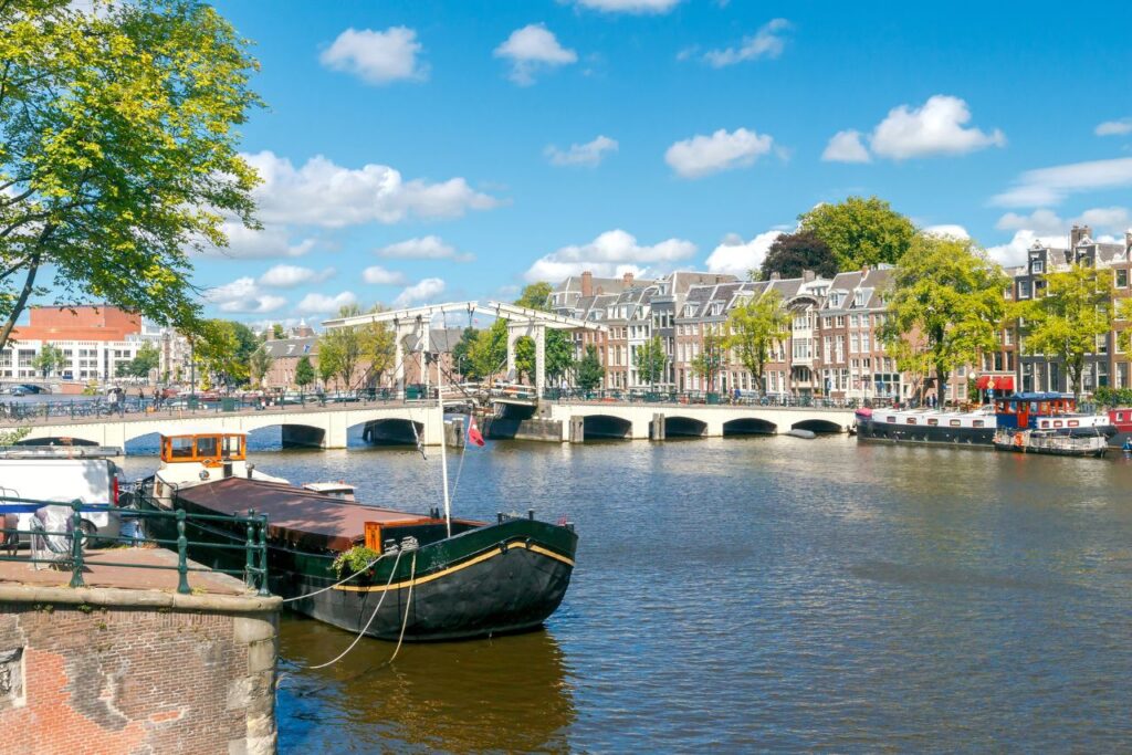 View of the canals of Amsterdam and the skinny bridge across the water with canal boats in front during your Amsterdam 3 day itinerary. 