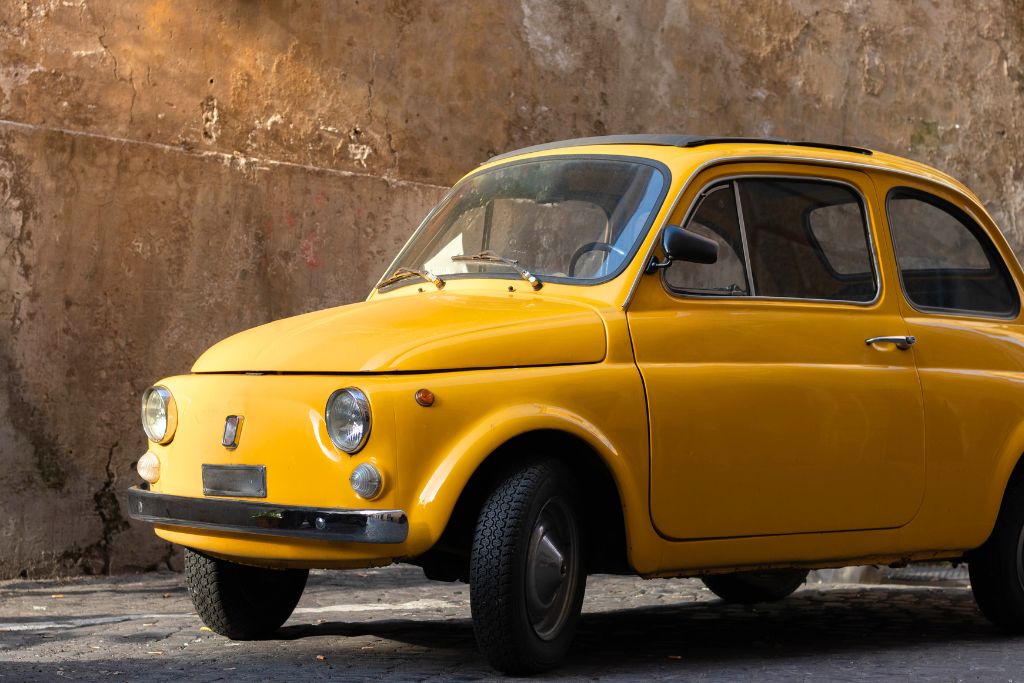 Vintage, yellow Fiat 500 parked on the street. 