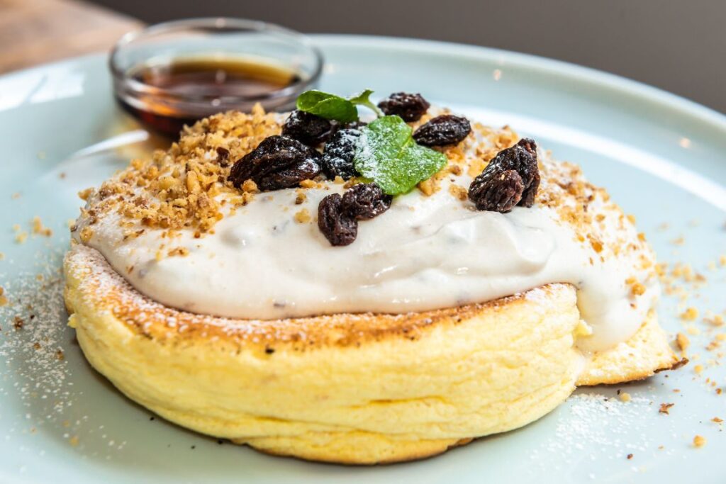 A light and fluffy Japanese pancake topped with sugar, raisins, and white sauce, with syrup on the side.