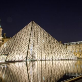 View of the glass pyramid in front of the Louvre all lit up in the evening during the best private tour of the Louvre
