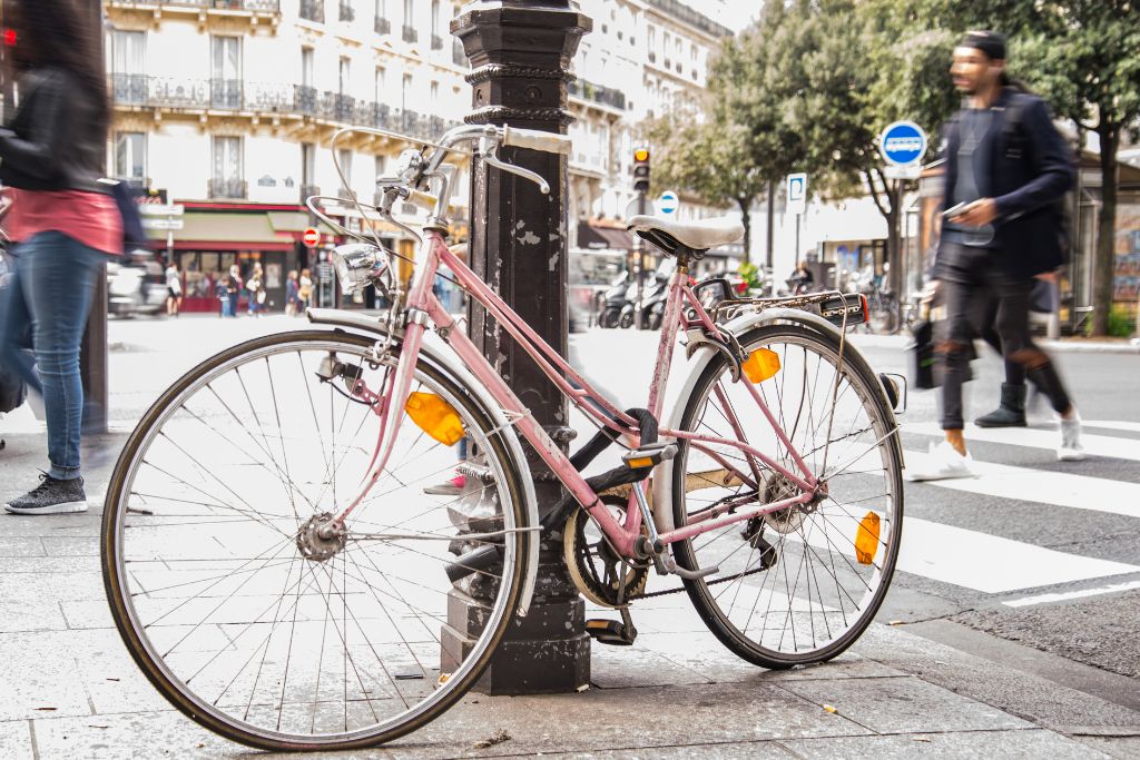 Pink bike sitting against a black post on a street in Paris. Use it to enjoy the best bike tours Paris has to offer. 
