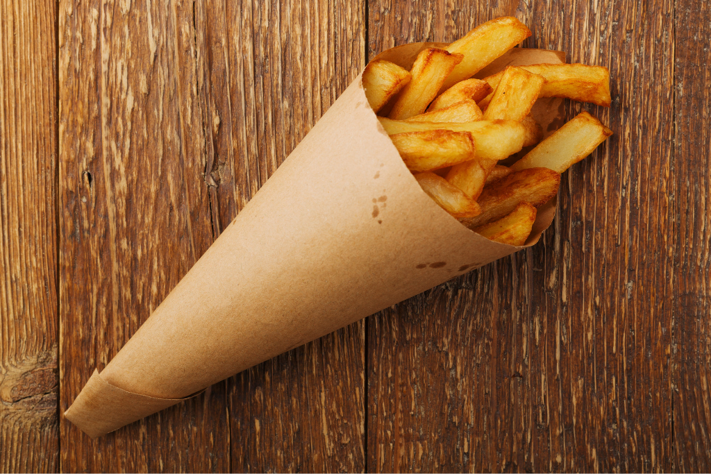 The best Belgian fries in Brussels are sitting in a brown paper cone on a wooden table. 